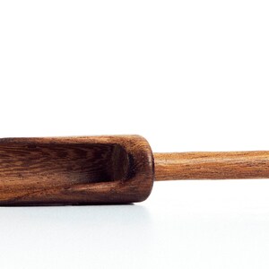 May include: A wooden scoop with a brown finish. The scoop has a shallow bowl and a long handle.