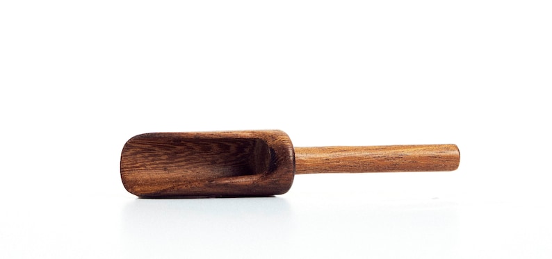 May include: A wooden scoop with a brown finish. The scoop has a shallow bowl and a long handle.