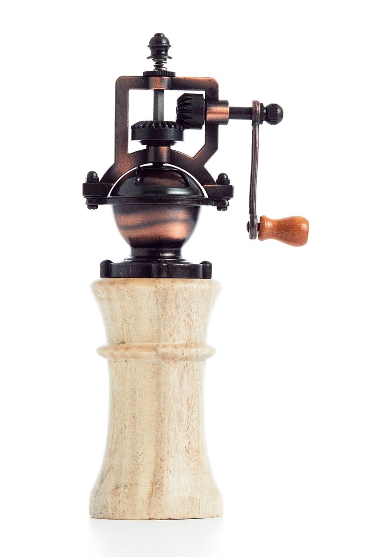 May include: A vintage-style manual pepper grinder with a wooden base and a metal grinding mechanism. The grinder has a crank handle and a copper-colored finish.