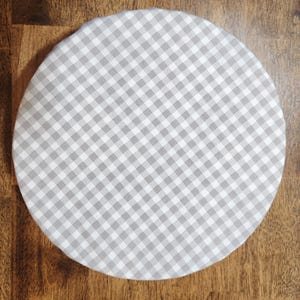 May include: A round, white tablecloth with a grey and white gingham pattern.