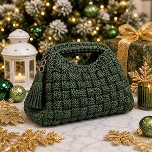 Può includere: Borsa a mano verde scuro intrecciata con manico e nappa. La borsa presenta un dettaglio a catena dorata. Lo sfondo include un albero di Natale, ornamenti e una confezione regalo.