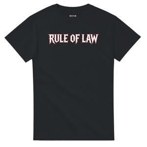 Op de afbeelding: Een zwart t-shirt met korte mouwen en de tekst RULE OF LAW in een wit lettertype met een dunne rode omlijning op de borst. Dezelfde tekst staat in een kleiner formaat op het label in de nek aan de binnenzijde van het kledingstuk.