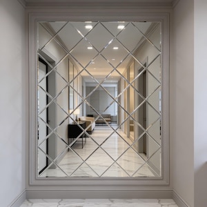May include: A large, rectangular wall mirror with a grid of diamond-shaped glass panels. The mirror is framed in a light gray molding and reflects a hallway with marble flooring and neutral-toned walls. The overall aesthetic is modern and elegant.