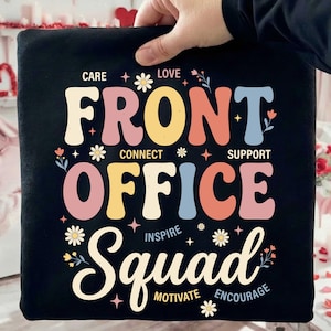 Könnte beinhalten: Schwarzes quadratisches Kissen mit dem Schriftzug "FRONT OFFICE Squad" in farbenfroher Retro-Schrift. Das Design enthält die Wörter "Care, Love, Connect, Support, Inspire, Motivate, Encourage" mit floralen Akzenten.