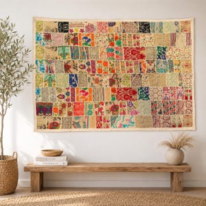 May include: A rectangular wall hanging featuring a patchwork design composed of numerous small, multi-coloured fabric squares. The textile displays a variety of intricate floral, paisley, and geometric patterns in shades of red, blue, green, and gold.