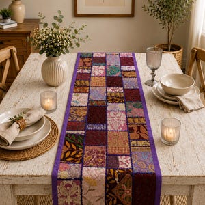 May include: A rectangular table runner featuring a patchwork design of various fabric squares in shades of purple, gold, pink, and maroon. The runner is bordered by a solid purple fabric trim and displays intricate embroidery and floral patterns.