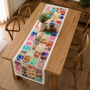 Pode incluir: Um caminho de mesa retangular longo com um design de patchwork vibrante, apresentando vários padrões florais e geométricos em tons de rosa, azul, amarelo, vermelho e verde, centrado numa mesa de jantar de madeira com rebordo branco.
