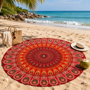 Könnte beinhalten: Ein großes, rundes Strandtuch mit einem leuchtend roten, orangen und gelben Mandalamuster sowie detaillierten Blumen- und Paisley-Motiven. Dazu gehören eine geflochtene Strohtasche, ein weißes Tuch, ein beiger Sonnenhut und eine Kokosnuss.