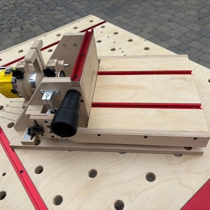 May include: A light-colored plywood router table featuring a yellow power tool motor, a black dust collection port, and red metal tracks. The assembly is mounted on a larger perforated workbench surface with matching red tracks and circular holes.