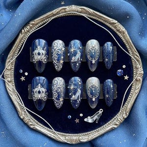 May include: A set of ten almond-shaped press-on nails featuring a deep navy blue and silver glitter finish. The designs include a silver carriage, intricate silver swirls, a light blue glass slipper, a clock face set to midnight, and small stars.