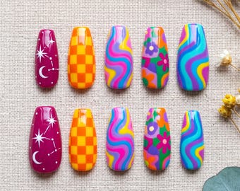 May include: A set of ten press-on nails featuring various colorful designs including a deep magenta base with white celestial stars and moons, an orange and yellow checkerboard pattern, multi-colored wavy lines, and a floral print with green.