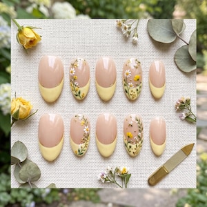 Pode incluir: Um conjunto de dez unhas postiças ovais com base nude e pontas amarelo-pálido. Algumas unhas são decoradas com margaridas brancas pintadas à mão, caules verdes e pequenas abelhas amarelas. Inclui uma lixa de unhas de metal dourado.