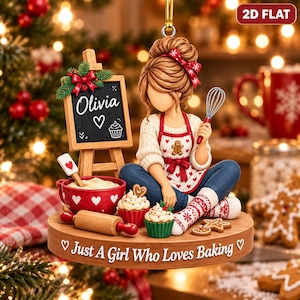 May include: A flat Christmas ornament featuring a figure with a bun hairstyle wearing a heart-patterned apron, holding a whisk. Beside them is a chalkboard sign reading Olivia with a heart and cupcake, a red bowl, and text Just A Girl Who Loves Baking.