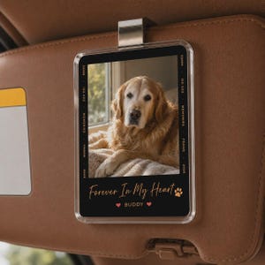 May include: A clear acrylic car visor clip featuring a photo of a golden retriever. The frame includes text reading 35MM, ISO 400, MEMORIES, FRAME, 2026, and Forever In My Heart, BUDDY with a paw print and two small heart icons.