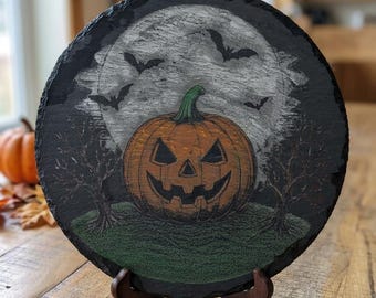 May include: A round black slate plaque featuring a hand-painted Halloween scene with a central orange jack-o'-lantern, a large white full moon, silhouetted bats, and bare trees on a green grassy patch, displayed on a dark wooden stand.