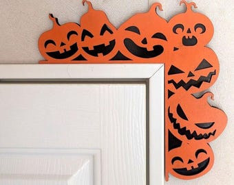 May include: A decorative orange door corner accent featuring a series of carved jack-o'-lantern pumpkins with black cut-out eyes, noses, and mouths. The L-shaped piece is designed to fit around the top corner of a door frame, displaying various expressions.