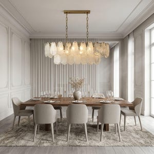 May include: A rectangular chandelier featuring multiple translucent, oval-shaped glass pieces suspended from a brass-toned metal frame. The fixture is hung by two chains and contains internal light bulbs that emit a warm glow through the textured glass.