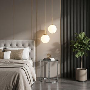 Può includere: Due lampade a sospensione sferiche in vetro bianco con supporti in metallo dorato pendono dal soffitto. Le lampade presentano un design liscio e rotondo che emette una luce calda, sospese ad altezze diverse sopra un tavolino circolare.
