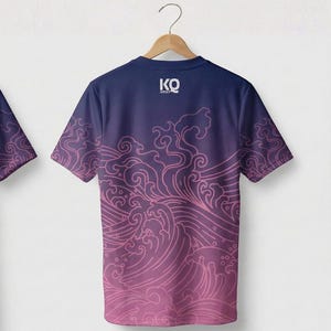 Op de afbeelding: Marineblauw T-shirt met een roze golfpatroon. Het shirt heeft korte mouwen en de tekst "KO JERSEY" bovenaan. Het golfpatroon vervaagt van roze naar marineblauw.
