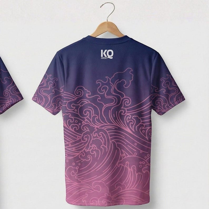Op de afbeelding: Marineblauw T-shirt met een roze golfpatroon. Het shirt heeft korte mouwen en de tekst "KO JERSEY" bovenaan. Het golfpatroon vervaagt van roze naar marineblauw.