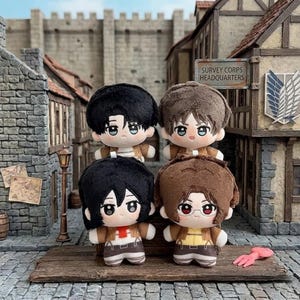 Op de afbeelding: Vier pluche poppen met anime-achtige kenmerken, elk met verschillende kapsels en outfits. De poppen staan op een houten oppervlak voor een miniatuur stadsgezicht. De poppen hebben bruin en zwart haar en dragen bruine jassen en beige broeken.