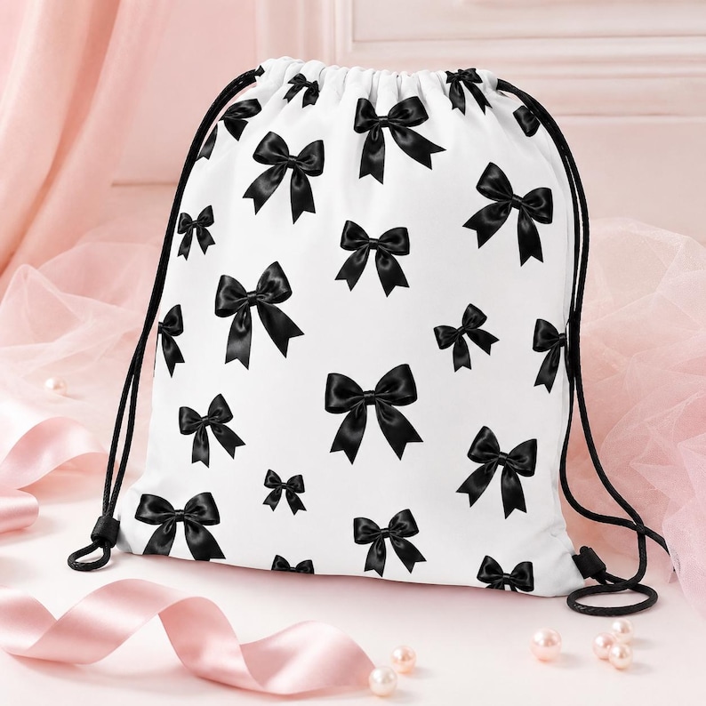 Peut inclure: Sac de sport blanc avec un motif r&eacute;p&eacute;t&eacute; de n&oelig;uds noirs. Le sac a des cordons noirs et une fermeture noire. Le fond est un tissu rose tendre avec des perles et un ruban rose.