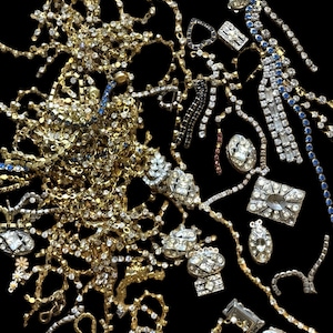 Puede incluir: Un surtido de piezas de joyería brillantes, que incluyen collares, pulseras y adornos individuales, se dispersan sobre un fondo negro. La joyería presenta pedrería transparente y metal dorado y plateado.