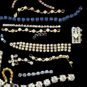 Puede incluir: Un surtido de piezas de joyería vintage, que incluyen cadenas de pedrería, pulseras y elementos decorativos. Las piezas presentan pedrería transparente, azul y roja engastada en metal dorado. También es visible un colgante en forma de corazón con pedrería roja.