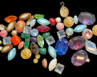 Könnte beinhalten: Eine Sammlung verschiedener loser Vintage-Cabochons und facettierter Strasssteine in unterschiedlichen Formen wie Marquise, Oval, Quadrat und Rund. Die Steine weisen eine vielfältige Farbpalette auf, darunter Blau, Rosa, Grün, Orange und Klarglas.