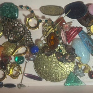 May include: A selection of vintage jewellery components and decorative elements in various shapes, sizes, and colours. Includes gold-toned filigree pieces, faceted gems, beads, and ornate metal findings. A mix of materials and styles.