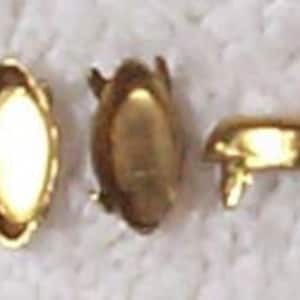 Könnte beinhalten: Drei goldfarbene, ovale, dekorative Metallverzierungen mit einem erhöhten Rand. Die Verzierungen haben vier kleine Füße an der Unterseite.