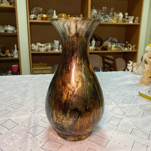 May include: A decorative vase with a wide, flared top and a bulbous body. The vase features a metallic finish with shades of brown, gold, and bronze, creating a textured, dripped effect. The vase is a decorative home accent.