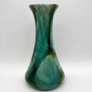 May include: A tall, green ceramic vase with a flared top and a rounded base. The vase has a glossy finish with shades of teal, dark green, and hints of yellow. The design features a flowing, organic pattern.