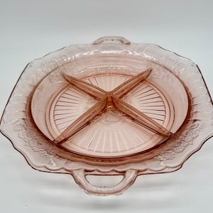 May include: A vintage pink glass divided serving dish. The dish has a square shape with rounded edges and two handles. It features a central section divided into four compartments by glass dividers. Floral detailing decorates the rim.