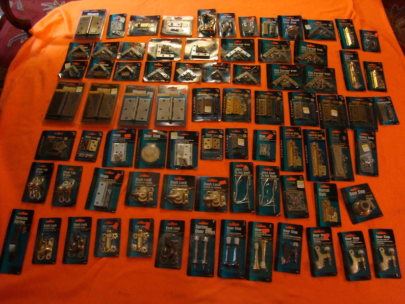 May include: A selection of door hardware in individual packaging, including hinges, door stops, door latches, and corner braces. The hardware is in various finishes, including brass, silver, and black.