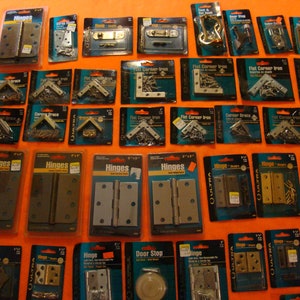 May include: An assortment of hardware items in individual packaging, including hinges, corner braces, flat corner irons, and door stops. The packaging is blue and white with the brand name "QULTRA" printed on it.