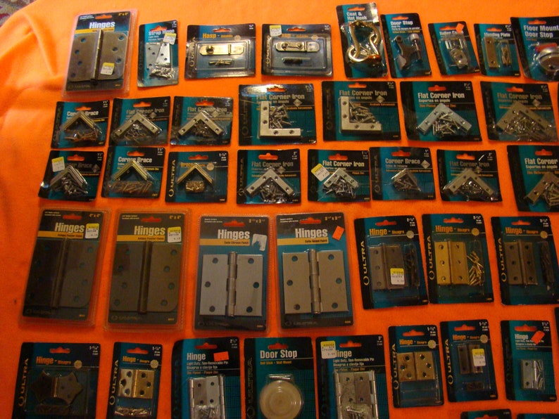 May include: An assortment of hardware items in individual packaging, including hinges, corner braces, flat corner irons, and door stops. The packaging is blue and white with the brand name "QULTRA" printed on it.