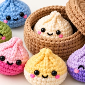 Könnte beinhalten: Eine Sammlung von sechs gehäkelten Knödel-Plüschfiguren mit lächelnden Gesichtern, schwarzen Perlenaugen und rosa gestickten Wangen. Die Knödel sind blau, grün, rosa, gelb und lila, wobei ein cremefarbener Knödel in einem braunen Häkelkorb liegt.
