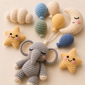 May include: A collection of crocheted items including a gray elephant, two yellow stars with smiling faces, a crescent moon with a sleeping face, a white cloud, and five small balloons in blue, cream, yellow, and green, all connected by white strings.