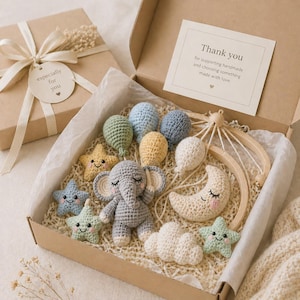 May include: A gift box containing a crochet baby mobile kit with a gray elephant, a cream moon, white clouds, and colorful balloons and stars. A card inside reads: Thank you for supporting handmade and choosing something made with love.