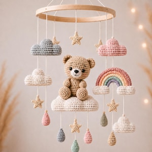 Puede incluir: Móvil de bebé hecho a mano con ganchillo, con un osito de peluche, nubes, estrellas y un arcoíris. El móvil está suspendido de un aro de madera. El oso es marrón, las nubes son de varios colores y las estrellas son beige.