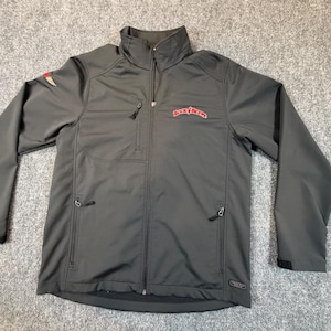 May include: A charcoal gray jacket with a full-length zipper, a stand-up collar, and multiple zippered pockets. The jacket features a red logo on the chest and a small emblem on the left sleeve. The jacket is made of a smooth, water-resistant material.