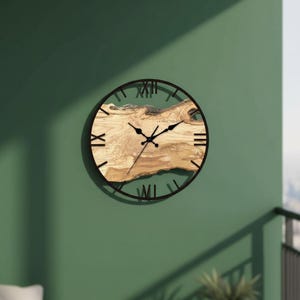 Könnte beinhalten: Eine runde Wanduhr mit einem dunkelbraunen Metallrahmen und römischen Ziffern. Das Zifferblatt hat ein natürliches Holzmaserungsdesign und schwarze Zeiger. Die Uhr ist an einer grünen Wand befestigt.
