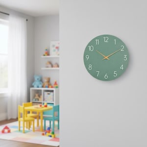 May include: A circular, sage green wall clock featuring white numerals and gold-coloured hands. The clock is mounted on a white wall. The clock's diameter is approximately 30 cm.