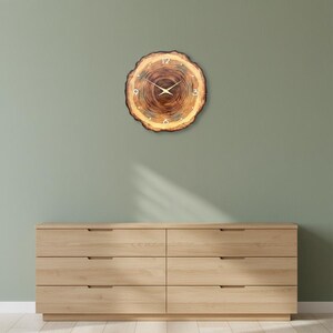 May include: A round wall clock made from a natural wood slice with visible tree rings and bark edges. The clock face features gold-coloured hands and gold-coloured numerals at the 12, 3, 6, and 9 o'clock positions, set against the brown wood grain.