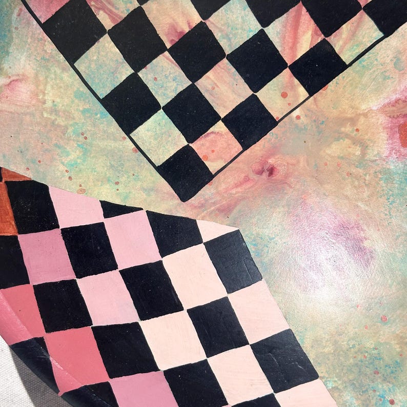 K&ouml;nnte beinhalten: Abstrakte Kunst mit zwei Schachbrettmustern in Schwarz und Rosa sowie Schwarz und Wei&szlig;. Der Hintergrund hat einen Aquarelleffekt mit rosa, blauen und gelben Farbt&ouml;nen. Die Komposition ist eine Nahaufnahme der bemalten Oberfl&auml;che.