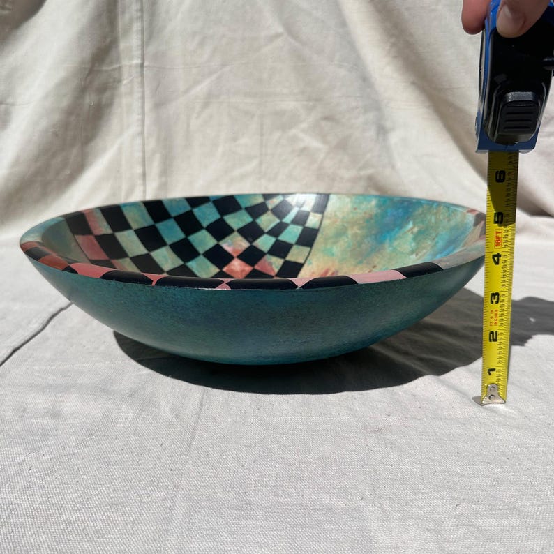 K&ouml;nnte beinhalten: Eine t&uuml;rkisfarbene dekorative Sch&uuml;ssel mit einem Schachbrettmuster in Schwarz, T&uuml;rkis und Rosa. Die Sch&uuml;ssel hat einen Durchmesser von ca. 15 cm und ein einzigartiges, k&uuml;nstlerisches Design. Die Sch&uuml;ssel besteht aus einem gl&auml;nzenden Material.