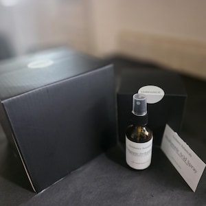 May include: A dark amber glass bottle with a spray nozzle, a black box, and a white tag. The bottle is labeled "Verdance Botanicals" and "Hyaluronic Acid Spray". The box has a white circular sticker.