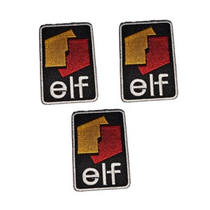 Puede incluir: Tres parches bordados con la palabra "elf" en blanco. Cada parche tiene un fondo negro con un diseño geométrico dorado y rojo. Los parches son rectangulares con un borde negro.