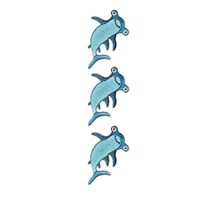 May include: Three identical embroidered hammerhead shark patches arranged vertically. Each patch features a light blue belly, dark blue fins and tail, and a smiling face with two round eyes on the sides of the hammer-shaped head.